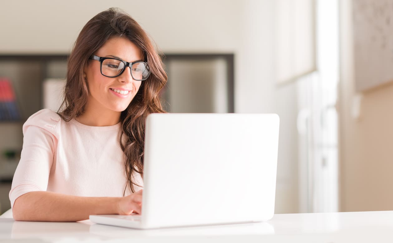 A woman smiles and types at her laptop.